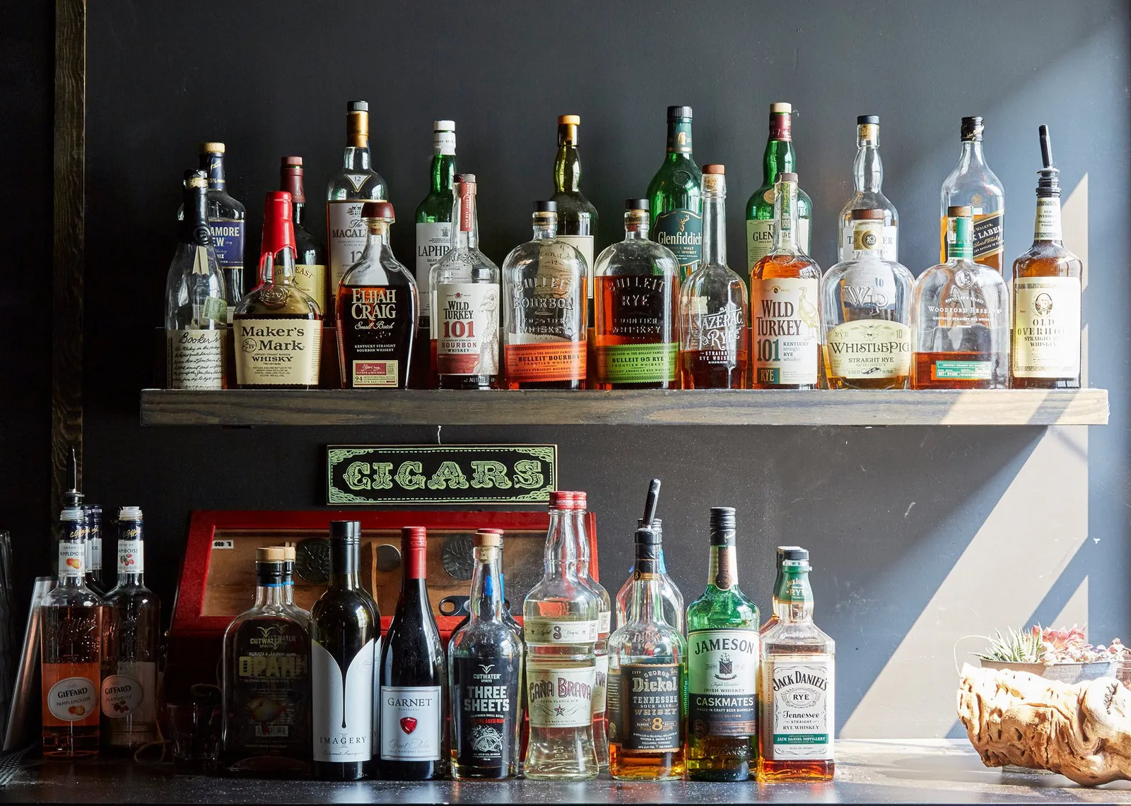 Bottles and a Cigars sign on the back bar shelf