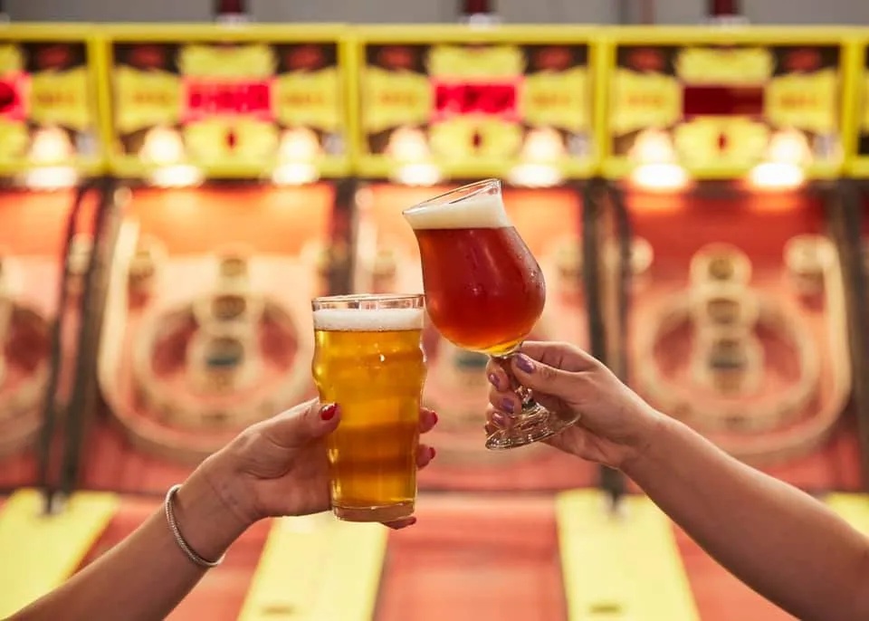 Two pints clinking in front of the Skeeball lanes