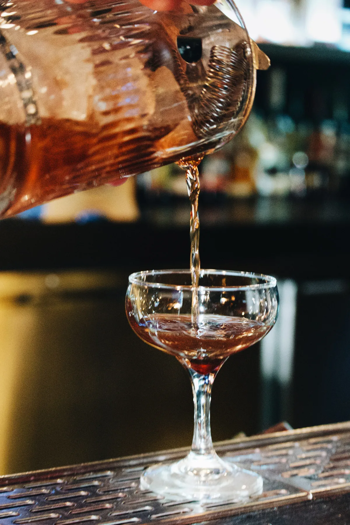 A cocktail being poured into a coupe