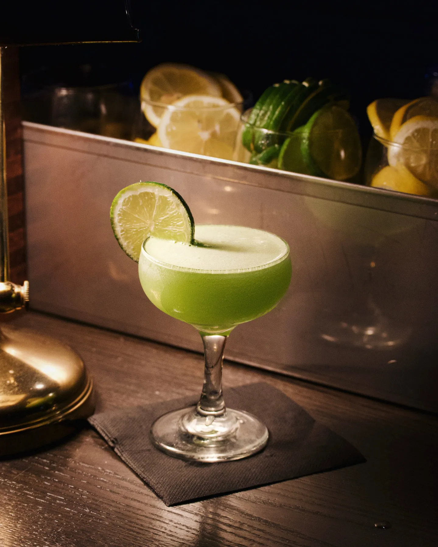 A pale green cocktail with a lime wheel